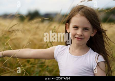 Mignonne belle petite fille aux cheveux roux sans dents sur le fond d'un champ de blé et d'une route rurale. Concept de voyage pour enfants Banque D'Images