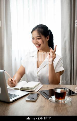 Une belle et heureuse professeure asiatique en ligne enseigne à ses élèves en ligne, travaillant à distance depuis la maison. Une femme d'affaires ayant une réunion en ligne. Banque D'Images