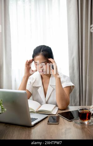 Une jeune femme d'affaires asiatique stressée est assise à son bureau dans le bureau, confrontée à des problèmes, profondément dans la pensée, la réflexion et la planification de la façon de les résoudre. Banque D'Images