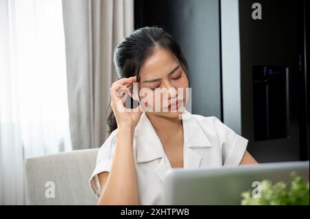 Une jeune femme d'affaires asiatique stressée est assise à son bureau dans le bureau, confrontée à des problèmes, profondément dans la pensée, la réflexion et la planification de la façon de les résoudre. Banque D'Images