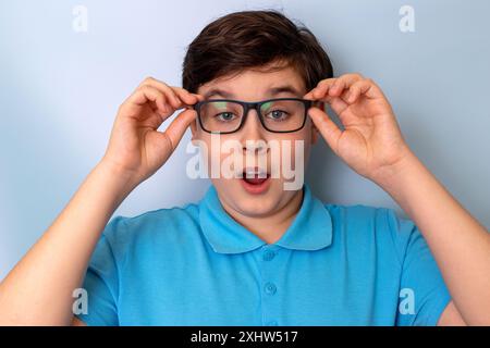 Un beau garçon surpris, aux cheveux foncés, portant des lunettes et un T-shirt bleu, Banque D'Images