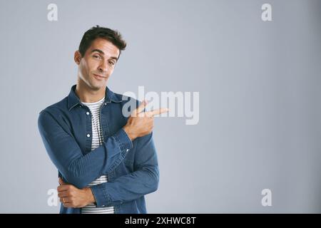 Portrait, pointage et homme avec revue, information et modèle sur fond gris de studio. Visage, personne et gars avec geste de la main, espace maquette et Banque D'Images