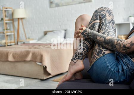 Une jeune femme avec des tatouages complexes est assise sur un canapé dans son appartement moderne, profitant d'un week-end confortable. Banque D'Images