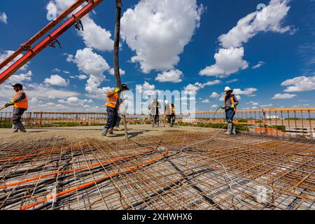 Le travailleur de la construction dans des bottes en caoutchouc dirige le tube de pompe dans la bonne direction, versant la couche de béton, nivelant le ciment sur l'armature carrée. T Banque D'Images