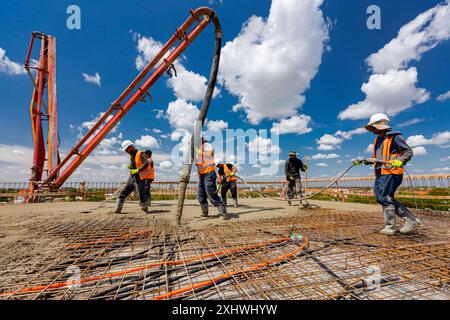 Le travailleur de la construction dans des bottes en caoutchouc dirige le tube de pompe dans la bonne direction, versant la couche de béton, nivelant le ciment sur l'armature carrée. T Banque D'Images