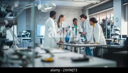 Jeunes ingénieurs travaillant dans le laboratoire des installations de l'entreprise : Groupe de spécialistes internationaux de laboratoires multiethniques réunis autour d'une table pour discuter des plans et des composants d'un projet robotique de haute technologie Banque D'Images