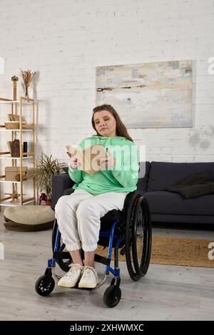 Une jeune femme brune est assise dans un fauteuil roulant dans son salon, englouti dans la lecture d'un livre. Banque D'Images