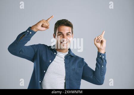 Portrait, pointage et homme avec revue, excité et modèle sur fond gris de studio. Visage, personne et mec avec geste de la main, espace de maquette ou promotion Banque D'Images