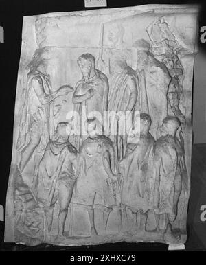 Relief montrant un chef germanique avec un groupe de barbares se rendant en plaçant une main sur la poitrine, tandis que l'empereur tient un rouleau, illustrant le geste et la hiérarchie. Banque D'Images