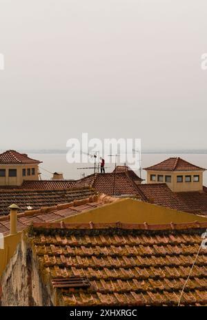 Un homme se tient au sommet des toits de tuiles rouges à Alfama, surplombant le fleuve Tage Banque D'Images