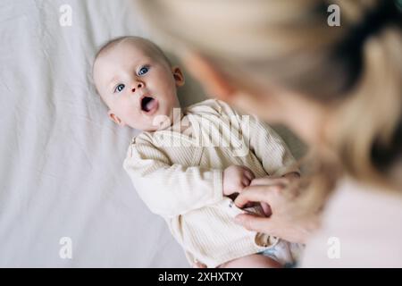 Maman change le body d'un bébé mignon joyeux après avoir changé la couche. Banque D'Images