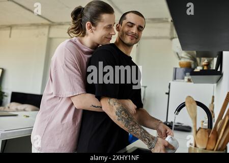 Un jeune couple gay montre de l'affection tout en faisant la vaisselle dans leur cuisine moderne. Banque D'Images