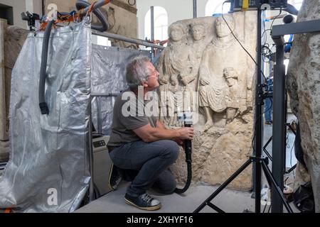 Mainz, Allemagne. 16 juillet 2024. Le restaurateur Mathias Steyer travaille sur la pierre dite de Blussus, une pierre tombale de l'époque romaine. La pierre tombale d'un Celte, qui est représentée avec sa femme Menimane sur un côté de la pierre et montre une inscription et la représentation d'un navire du Ier siècle sur l'autre côté, a été trouvée à Mayence-Weisenau. Crédit : Helmut Fricke/dpa/Alamy Live News Banque D'Images