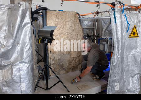 Mainz, Allemagne. 16 juillet 2024. Le restaurateur Mathias Steyer travaille sur la pierre dite de Blussus, une pierre tombale de l'époque romaine. La pierre tombale d'un Celte, qui est représentée avec sa femme Menimane sur un côté de la pierre et montre une inscription et la représentation d'un navire du Ier siècle sur l'autre côté, a été trouvée à Mayence-Weisenau. Crédit : Helmut Fricke/dpa/Alamy Live News Banque D'Images