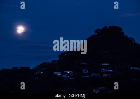 Les lumières des maisons construites sur le flanc du Mont Paku comme une pleine lune se lève au-dessus de la péninsule de Coromandel sur l'île du Nord de la Nouvelle-Zélande Banque D'Images