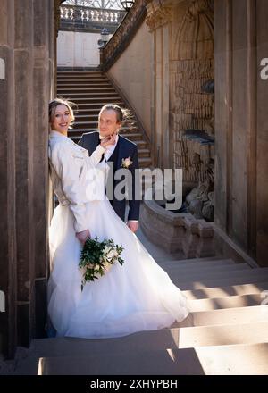 Portrait de mariage. La mariée s'appuie contre un mur de pierre et regarde dans la caméra, le marié la regarde avec amour. Banque D'Images