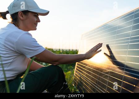 Femme touche un panneau solaire au coucher du soleil. Banque D'Images