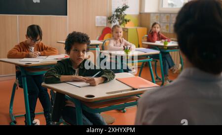 Groupe de leçon de classe d'école de diversité multiraciale enfants multiethniques enfants étudiant l'apprentissage lever mains méconnaissable enseignante vue arrière Banque D'Images