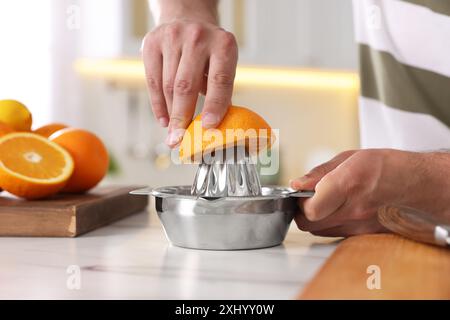 Homme pressant l'orange fraîche avec presse-agrumes à la table en marbre blanc, gros plan Banque D'Images