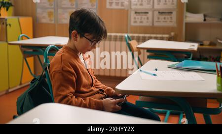 Éducation scolaire étudier Caucasien garçon petit fils écolier enfant élève élève écolier garçon à la leçon de classe gadget addict dépendance au téléphone portable Banque D'Images