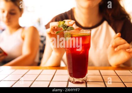 Gros plan d'un verre avec un délicieux cocktail frais à la menthe et au citron vert sur la table. Une fille boit une boisson savoureuse aux agrumes avec de la glace dans un café insi Banque D'Images