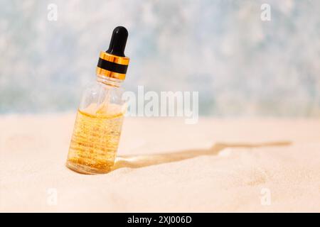 Maquette de bouteille de cosmétiques avec pipette et liquide transparent avec des particules d'or sur sable. Essence de crème solaire avec des vitamines dans un tube de verre. Moisturi Banque D'Images