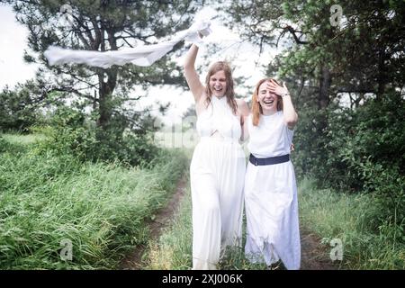 Deux charmantes filles en robes blanches courent sous la pluie d'été. Les jeunes femmes insouciantes rient et apprécient la pluie. Les amies féminines attirantes l'ont Banque D'Images