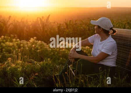 Femme portant un chapeau blanc est assis à côté du panneau solaire au coucher du soleil. Banque D'Images