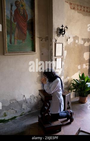 Femme chrétienne priant dans une petite chapelle de rue à Volterra, Toscane, Italie Banque D'Images