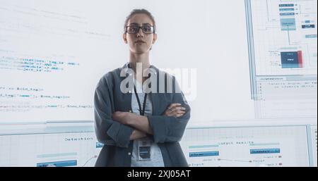 Portrait de femme regardant la caméra, croisant les bras avec de grands écrans numériques glitching dans l'arrière-plan. Pirate professionnel féminin posant après avoir percé le système de protection de cybersécurité. Banque D'Images