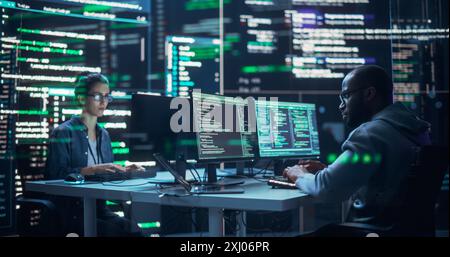Portrait de deux développeurs divers travaillant sur des ordinateurs, en tapant des lignes de code qui apparaissent sur les grands écrans qui les entourent. Programmeurs masculins et féminins créant des logiciels innovants, corrigeant des bugs. Banque D'Images