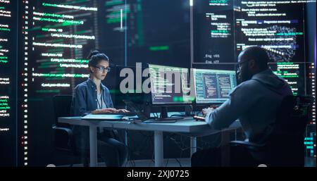 Portrait de deux programmeurs travaillant dans une salle de contrôle de surveillance, entourés de grands écrans affichant des lignes de code de langage de programmation. Portrait de divers développeurs créant un logiciel, codage Banque D'Images