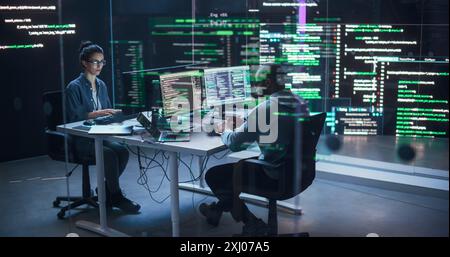 Portrait deux développeurs divers travaillant sur des ordinateurs, tapant des lignes de code qui apparaissent sur les grands écrans qui les entourent. Programmeurs masculins et féminins créant des logiciels innovants, corrigeant des bugs Banque D'Images