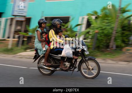 Une famille à moto à Hikkaduwa, Sri Lanka. Un adulte conduit tandis que deux enfants et un autre adulte conduisent en tant que passagers Banque D'Images