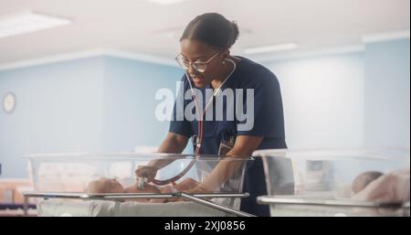 Happy Professional infirmière fournissant des soins 24 heures sur 24 à un bébé prématuré récupéré dans une unité de soins intensifs néonatals. Médecin féminin africain vérifiant sur un enfant, en utilisant stéthoscope dans la clinique de la pépinière Banque D'Images