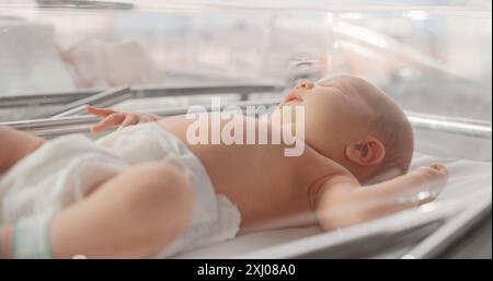 Mère attentive changeant la couche pour un nouveau-né. Enfant nouveau-né allongé dans un berceau d'hôpital dans une clinique de pépinière. Maternité, enfance et concept médical Banque D'Images