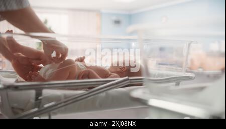 Mère attentive changeant la couche pour un nouveau-né. Enfant nouveau-né allongé dans un berceau d'hôpital dans une clinique de pépinière. Maternité, enfance et concept médical Banque D'Images