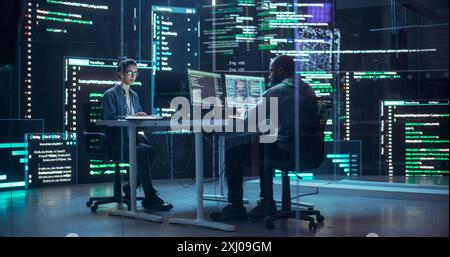 Portrait deux développeurs divers travaillant sur des ordinateurs, tapant des lignes de code qui apparaissent sur les grands écrans qui les entourent. Programmeurs masculins et féminins créant ensemble des logiciels innovants, corrigeant des bugs Banque D'Images