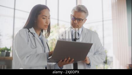 Médecin asiatique professionnel et médecin d'âge moyen ayant une conversation dans un hôpital médical de soins de santé. Collègues utilisant un ordinateur portable, discutant du traitement du patient, des médicaments ou de la thérapie Banque D'Images