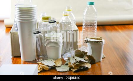 Tasse à café en papier blanc, papier usagé, bouteilles en plastique et boîte en carton sur une surface brune, en attente de recyclage. Favorise le recyclage des déchets, sauver l'oreille Banque D'Images