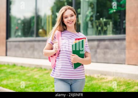 Photo d'adorable adorable Sweet Lady Wear t-shirt rayé sac d'école contenant des manuels scolaires profitant de la marche à l'extérieur de la rue urbaine de la ville Banque D'Images