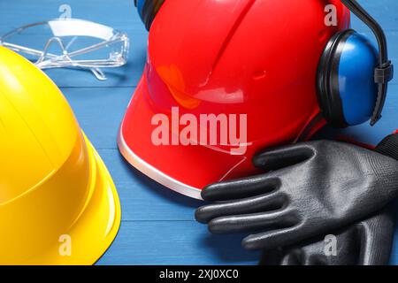 Casques de sécurité, gants de protection, protections auditives et lunettes sur fond de bois bleu, gros plan Banque D'Images