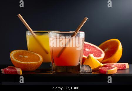 Verres de pamplemousse et jus d'orange avec de la glace sur un fond noir. Boissons rafraîchissantes avec des tranches de fruits. Banque D'Images