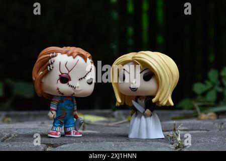 Funko Pop figurines de tueurs en série poupées Chucky et Tiffany des films d'horreur Child's Play. Cour sombre, clôture noire, ombres, vert sombre. Banque D'Images