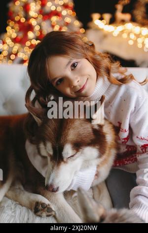 Gros plan de fille mignonne embrassant chien Husky sur fond de noël Banque D'Images