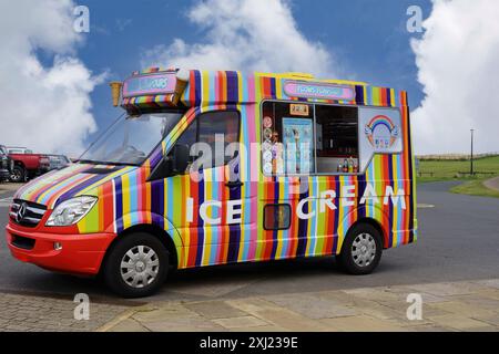 Un fourgon de crème glacée stationnaire avec un arc-en-ciel de rayures et une sélection alléchante de saveurs, Whitby, North Yorkshire, Royaume-Uni. Banque D'Images