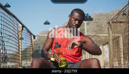 Image de nuages et d'icônes de flèche au-dessus de l'athlète masculin afro-américain tenant le temps de vérification de bouteille. Composite numérique, cloud computing, technologie, progr Banque D'Images