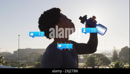 Image des icônes de notification et des chiffres sur l'homme afro-américain buvant de l'eau contre le ciel. Composite numérique, médias sociaux, technologie, exercice, f Banque D'Images