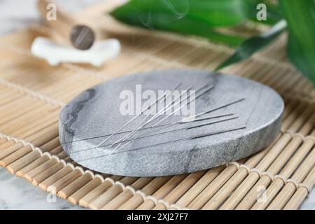 Dessous de verre en pierre grise avec aiguilles d'acupuncture sur tapis de bambou, gros plan Banque D'Images