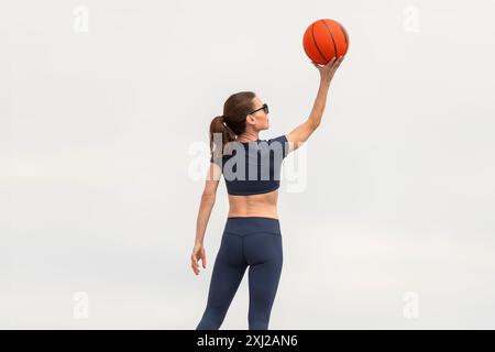 Femme sportive adulte de taille moyenne qui tire des paniers avec un ballon de basket-ball. Banque D'Images